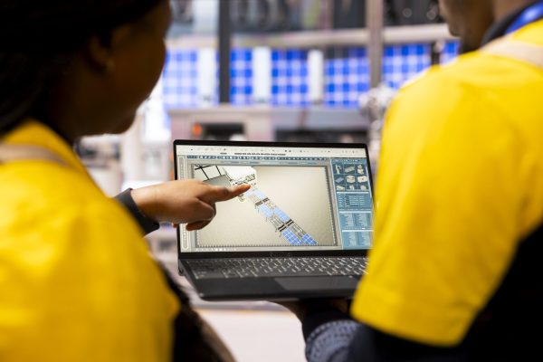 Smart factory experts use digital interface in optimization of industrial automation. Technicians review robotic assembly line and conveyor belt on laptop, enhancing efficiency in manufacturing plant.